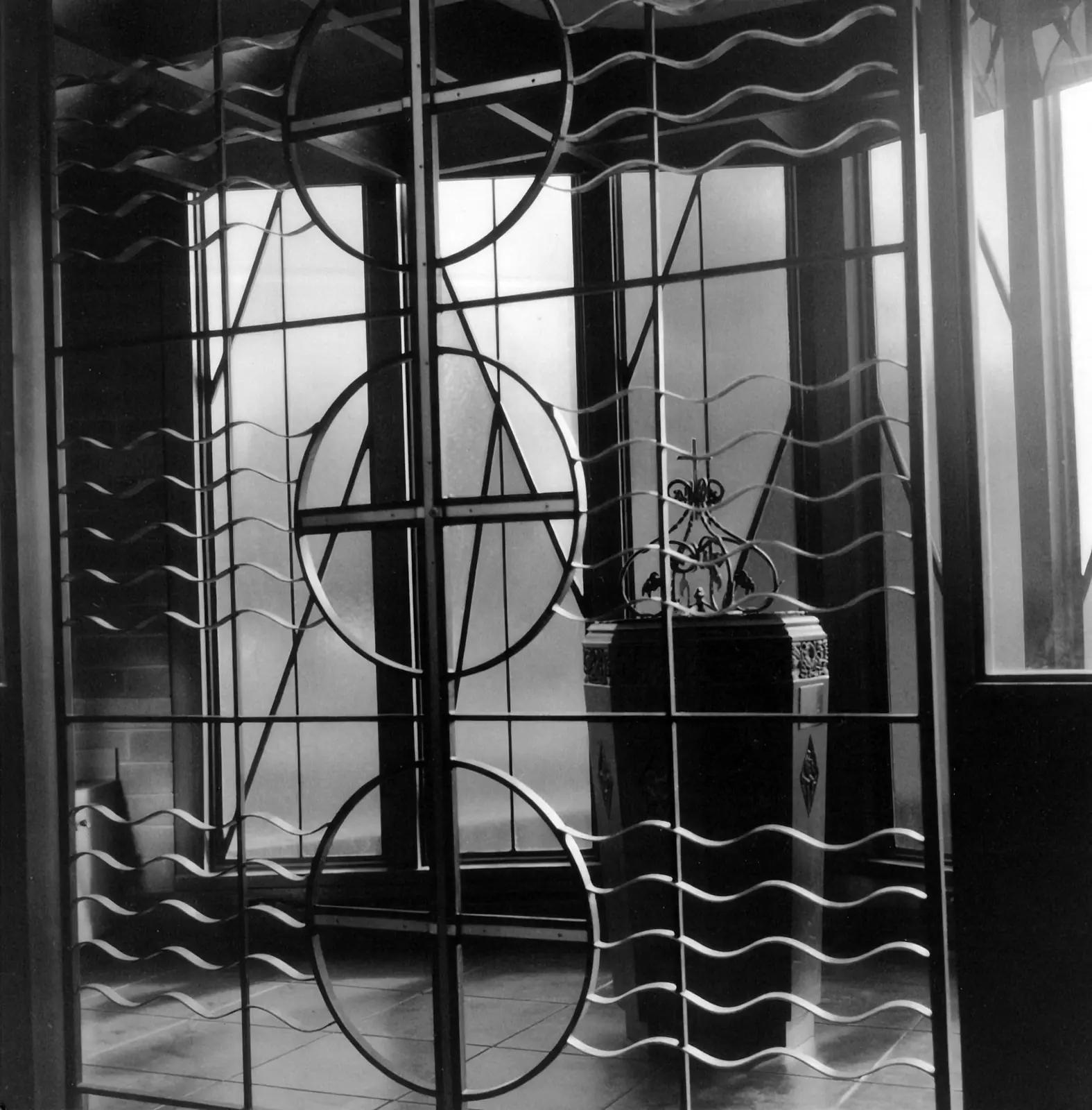 The brass-and-steel Baptistry Gate at St. Raymond, its wave motif symbolizing the waters of Baptism, with the baptismal font behind it.