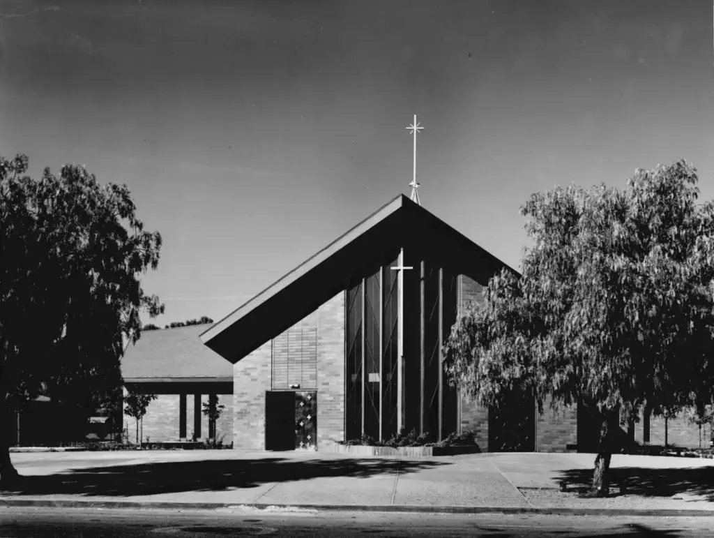 The A-frame front facade of St. Raymond Church, with its cross and tall glass, flanked by eucalyptus trees.